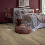 lichte beige eiken vloer met brede planken en subtiele houtnerfstructuur in een slaapkamer met een zachtroze wand, wit beddengoed en een gebreid plaid