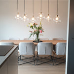 lichte beige eiken vloer met brede planken in rechte patroon onder een grote houten eettafel met zes lichtgrijze gestoffeerde eetkamerstoelen en hanglampen met glazen bolletjes erboven