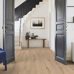 lichte vloer in breed plankmotief met natuurlijke houtstructuur en zachte beige eiken kleur in lichte, ruime hal met zwarte deuren en witte trap