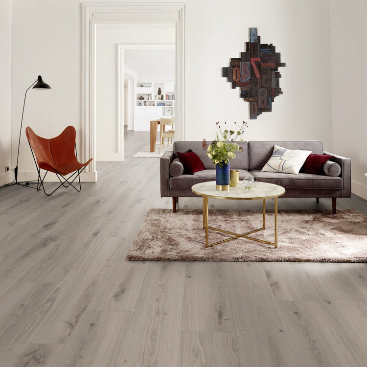 licht grijs eiken vloer met brede planken en subtiele houtnerfstructuur in moderne woonkamer met grijze bank, fijn tapijt in taupe en ronde marmeren salontafel met gouden frame