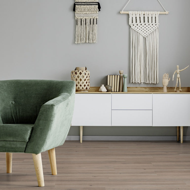 lichte beige eiken vloer met brede planken in rechte vloerpatroon onder een witte modern design dressoir met houten blad, groene fluwelen fauteuil en wanddecoratie van macramé en keramische accessoires