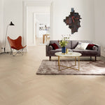 licht eiken vloer in visgraatpatroon met brede planken, grijs tapijt met zachte structuur, grijze bank met rode en witte kussens en gouden ronde salontafel met marmerlook blad in een modern witte woonkamer