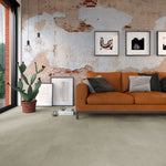 betonnen tegelvloer in licht beige met een matte, subtiel gegroefde structuur in een ruime moderne woonkamer met oranje bank en industrieel sobere muurdecoratie