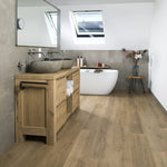 licht beige eiken vloer met brede planken in rechte patroon gecombineerd met taupe grote wandtegels, stenen waskommen op een massief houten wastafelmeubel, witte vrijstaande badkuip en droogboeket op houten kruk in moderne badkamer met dakraam