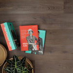 donkerbruin eiken vloer met lichte houtnerven en subtiele structuur, brede planken, met drie boeken en een groene plant op de vloer