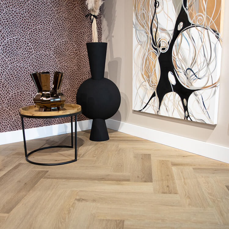 licht eiken visgraatvloer met subtiele houtnerfstructuur in een moderne interieurhoek met zwart metalen bijzettafeltje en zwarte decoratieve vaas naast abstract schilderij op beige muur