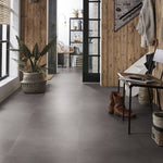 donkergrijze vloer met grote, matte tegels zonder patroon in lichte hal met houten wandbekleding en zwarte metalen deurkozijnen