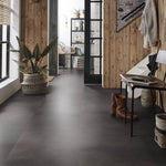 donkergrijze tegelvloer met grote, matte tegels zonder zichtbaar patroon in een hal met houten wandbekleding en plantenaccessoires