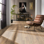lichte beige eiken vloer met brede planken en subtiele houtstructuur in modern interieur met bruine leren relaxstoel en zwarte metalen open kast tegen taupe muur