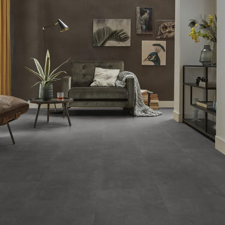 Antraciet tegelvloer met grote, matte tegels in effen patroon, gecombineerd met een donkergroen fluwelen fauteuil en een zwart metalen bijzettafeltje in moderne woonkamer.