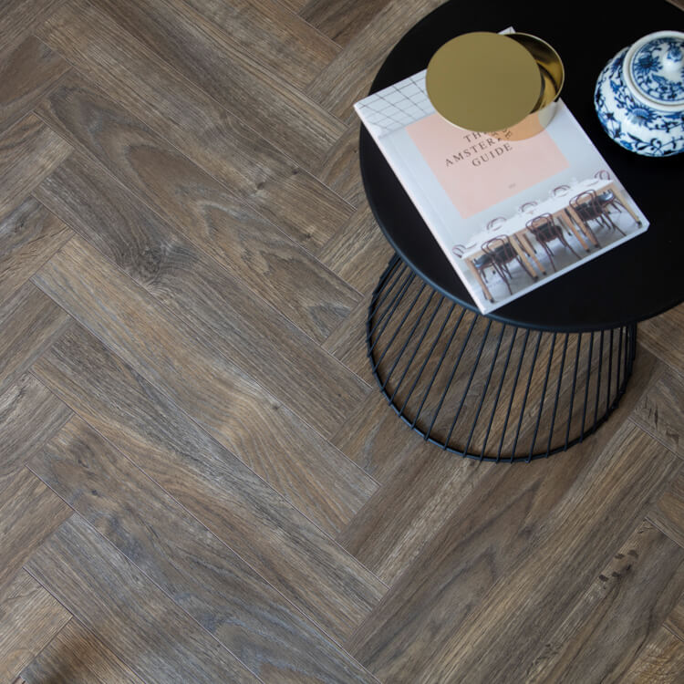 donker grijs bruin vloer met visgraatpatroon en fijne houtstructuur, zwart rond metalen bijzettafeltje met gouden decoratie en boek erop