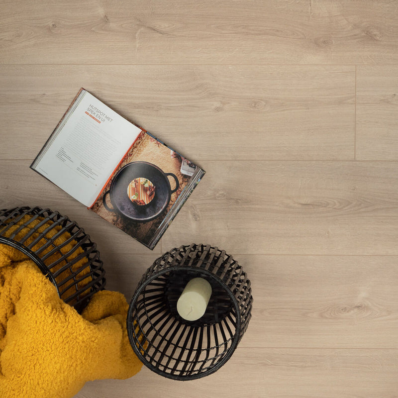 lichte beige eiken vloer met zichtbare houtnerf en brede planken, naast een open kookboek en een zwart gevlochten decoratief item met een witte kaars, en een gele zachte deken gedeeltelijk zichtbaar