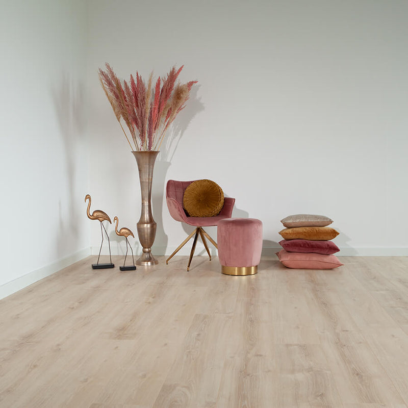 lichte eiken vloer met brede planken en subtiele houtnerfstructuur in een lichte beige tint, gestyled met een roze velvet draaistoel, een bijpassende poef met gouden voet, een stapel gekleurde kussens en een grote metalen vaas met pampagras naast twee bronzen flamingo-ornamenten