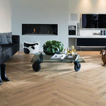 Licht beige eiken visgraatvloer met matte afwerking in moderne woonkamer met glazen salontafel op wielen en zwarte bank.