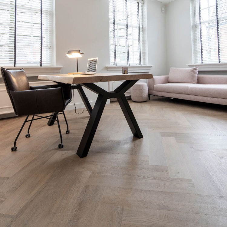 licht grijs eiken vloer met visgraat patroon in moderne werkruimte met houten tafel en zwart metalen onderstel, leren bureaustoel en lichtroze stoffen bank