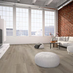 licht beige eiken vloer met brede planken en subtiele houtnerfstructuur in een lichte, moderne woonkamer met grote ramen, witte meubels en bakstenen muur