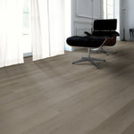 licht grijs eiken vloer met brede planken en subtiele houtstructuur in een moderne woonkamer met zwarte design fauteuil en grote ramen met witte gordijnen