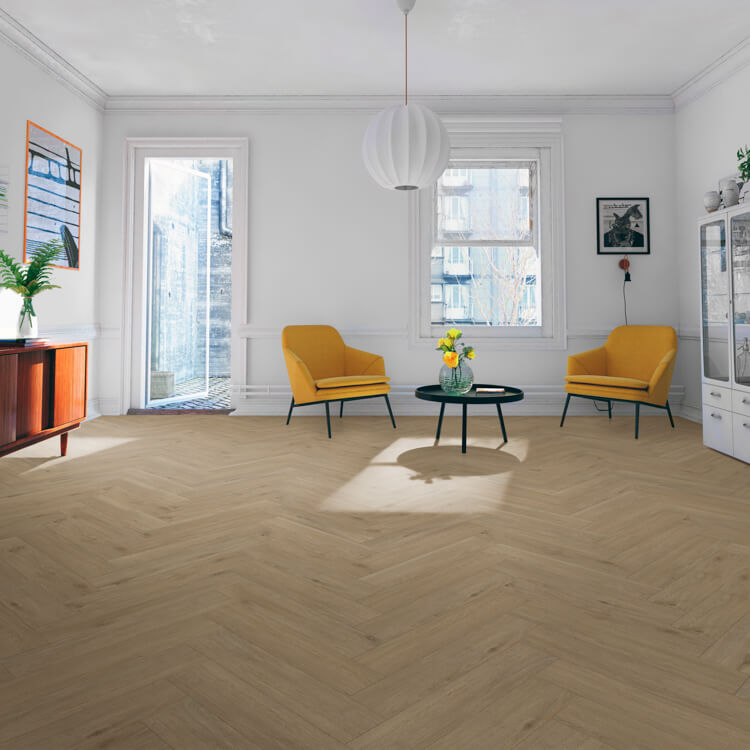 lichte beige eiken visgraatvloer met smalle planken in een lichte, ruime woonkamer met witte wanden, twee gele fauteuils en een zwarte ronde salontafel