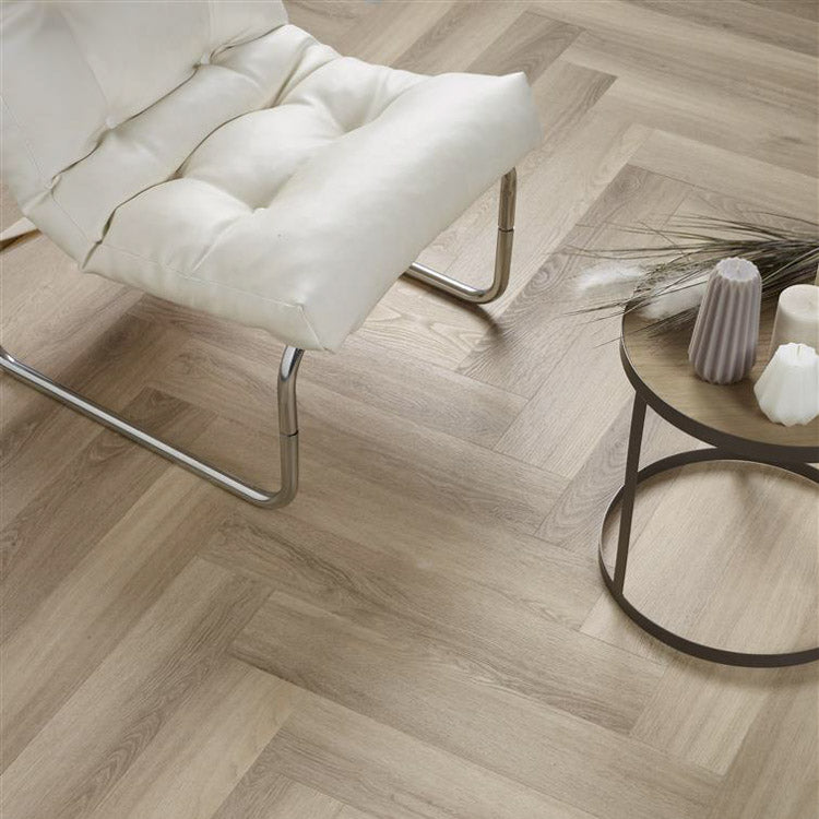 Licht eiken vloer met visgraatmotief en subtiele houtnerfstructuur, gecombineerd met een modern wit lederen fauteuil en een ronde salontafel met kaarsen in lichte pasteltinten.