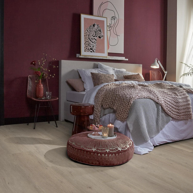 lichte beige eiken vloer met brede planken in een rustige slaapkamer met bordeauxrood geschilderde muur en zachte texturen zoals gebreide dekens en kussens
