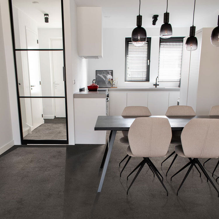 Donkergrijze tegelvloer met grote tegels en een subtiel golvend streeppatroon in een modern witte keuken met zwarte accenten en beige stoelen aan een zwartgrijze eettafel.