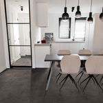 Donkergrijze tegelvloer met grote rechthoekige tegels en een subtiel golvend streeppatroon, gecombineerd met een modern interieur met licht beige eetkamerstoelen en een zwarte eettafel.