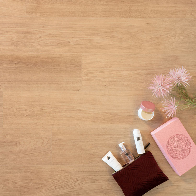 lichte eiken vloer met brede planken en subtiele houtnerfstructuur, met roze bloemen en diverse verzorgingsproducten naast een donkerrood stoffen tasje en een roze doosje