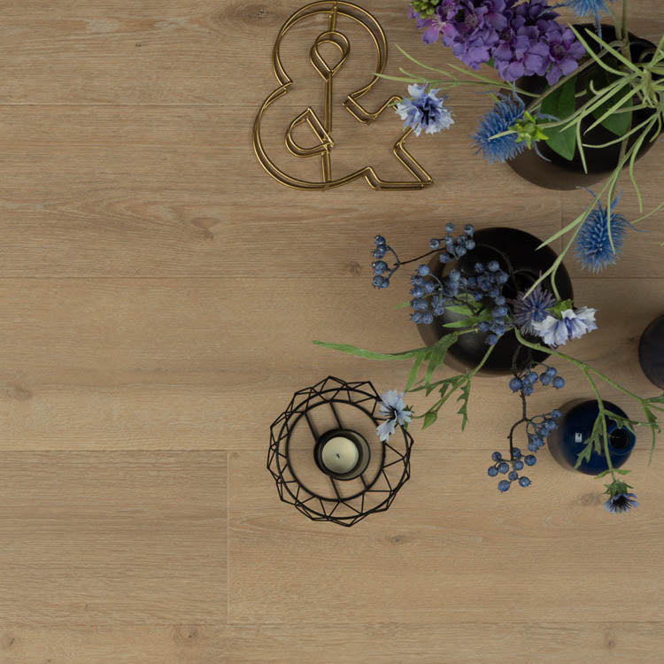 lichte beige eiken vloer met een subtiele houtstructuur en brede planken, bovenaanzicht met decoratieve bloemen in paars en blauw en een zwarte geometrische kaarshouder