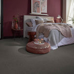 donkergrijs tapijt met fijne, gelijkmatige textuur in een slaapkamer met bordeauxrode muur, beige gebreide deken en neutrale bedlinnen