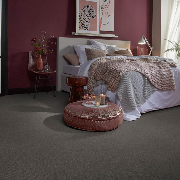 donkergrijs tapijt met fijne, gelijkmatige textuur in een slaapkamer met bordeauxrode muur, beige gebreide deken en neutrale bedlinnen