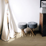 lichte beige eiken vloer met brede planken en een matte, natuurlijke structuur, twee ronde grijsblauwe gevlochten krukken met houten poten naast een witte wand en een houten kast