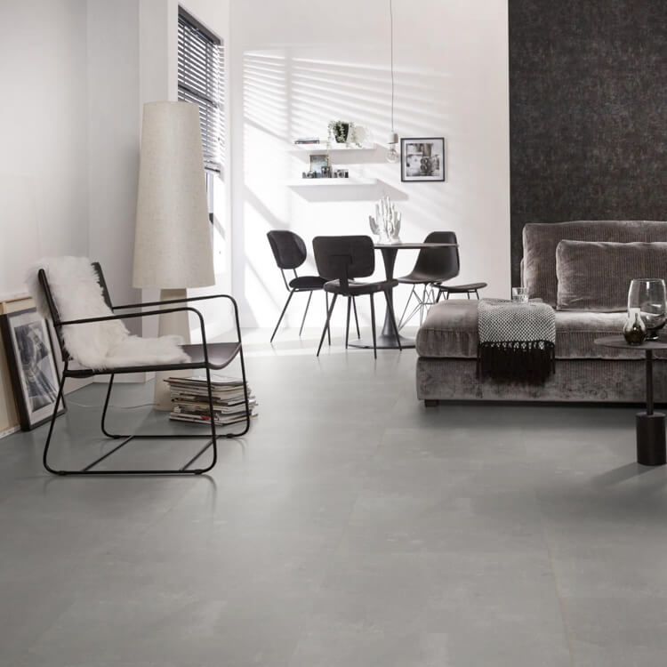 lichte tegelvloer met grote, matte tegels in zachtgrijs met subtiel golvend streeppatroon in modern ingerichte woonkamer met zwart metalen stoel, grijs fluwelen bank en ronde eettafel met zwarte stoelen