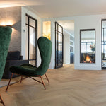licht eiken visgraatvloer met subtiele houtstructuur en brede planken in moderne woonkamer met groene velvet fauteuils en open haard