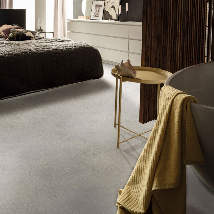 Licht grijze tegelvloer met subtiel golvend streeppatroon en matte structuur in moderne slaapkamer met losstaand bad en gouden bijzettafel