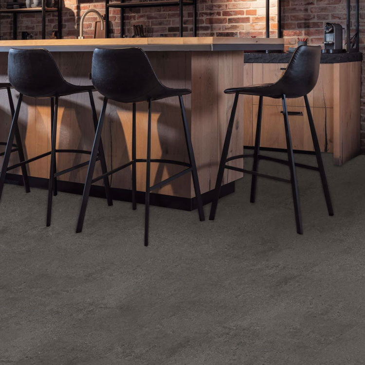 donkergrijze tegelvloer met subtiele betonstructuur in moderne keuken met zwart metalen barkrukken en houten keukenblad