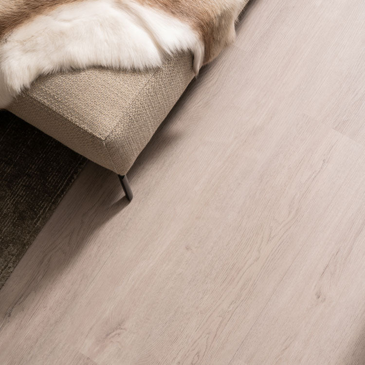 Lichte wit es vloer met een fijne houtnerfstructuur en brede planken, naast een licht beige stoffen bank met een bontkussen.