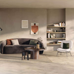 lichte vloer in visgraatpatroon met lichte beige eiken uitstraling, woonkamer met donkergrijze gebogen bank, houten ronde salontafel en beige vloerkleed