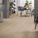 Licht eiken vloer met een subtiele houtnerfstructuur en brede planken in een natuurlijke, lichte beige tint, gecombineerd met modern interieur en zwart metalen stoelpoten.