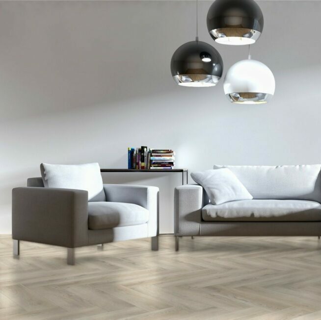 lichte vloer in visgraatpatroon met brede planken in licht wit es kleur, moderne zithoek met grijze stoffen bank en fauteuil, strakke witte muur en drie design hanglampen in zwart en wit met chromen binnenkant