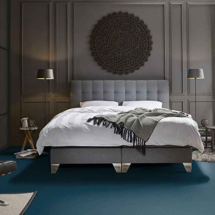 donkerblauwe matte vloer met een effen structuur in een moderne slaapkamer met grijze gestoffeerde boxspring en witte dekbedden, zwarte lampen en wanddecoratie in donkergrijs