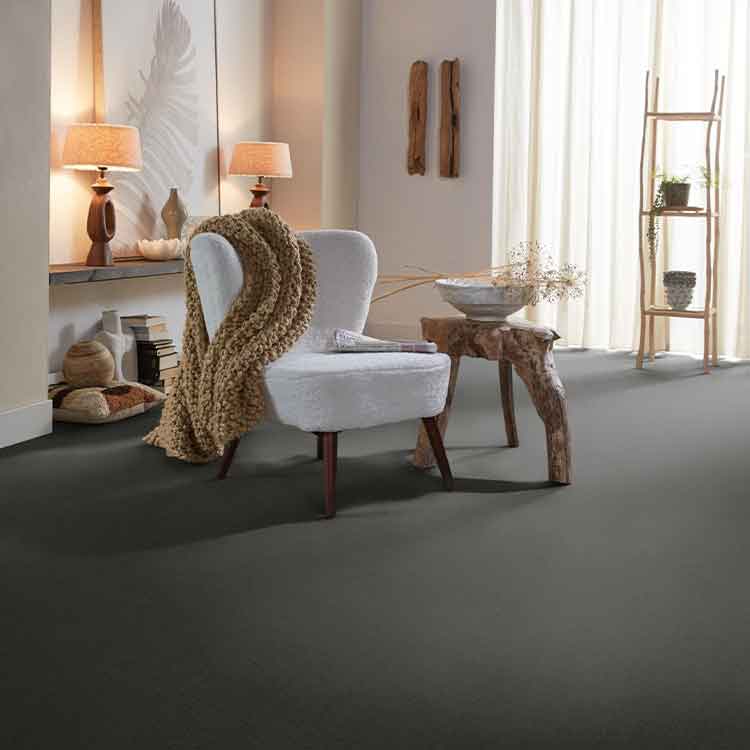 antracietgrijs tapijt met een effen, zachte structuur in een lichte, sfeervolle woonkamer met een lichtgrijze fauteuil en een robuuste houten salontafel