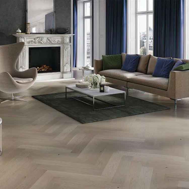 licht eiken visgraatvloer met matte afwerking in moderne woonkamer met beige bank, groene en blauwe kussens en wit marmeren salontafel op antraciet tapijt