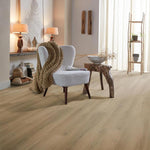 lichte beige eiken vloer met brede planken en subtiele houtnerfstructuur in een lichte, natuurlijke woonkamer met een wit stoffen stoel en een grove bruine gebreide plaid