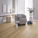 lichte beige eiken vloer met brede planken zonder opvallend patroon in moderne lichte woonkamer met grijze ronde fauteuil en witte accessoires