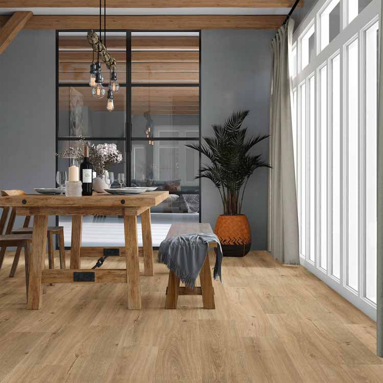 lichte houtkleurige vloer met brede planken in naturel kleur, robuuste houten eettafel met bankje en stoelen, grijs blad op bankje, grote plantenpot met groene palmplant naast grote ramen met lichtinval