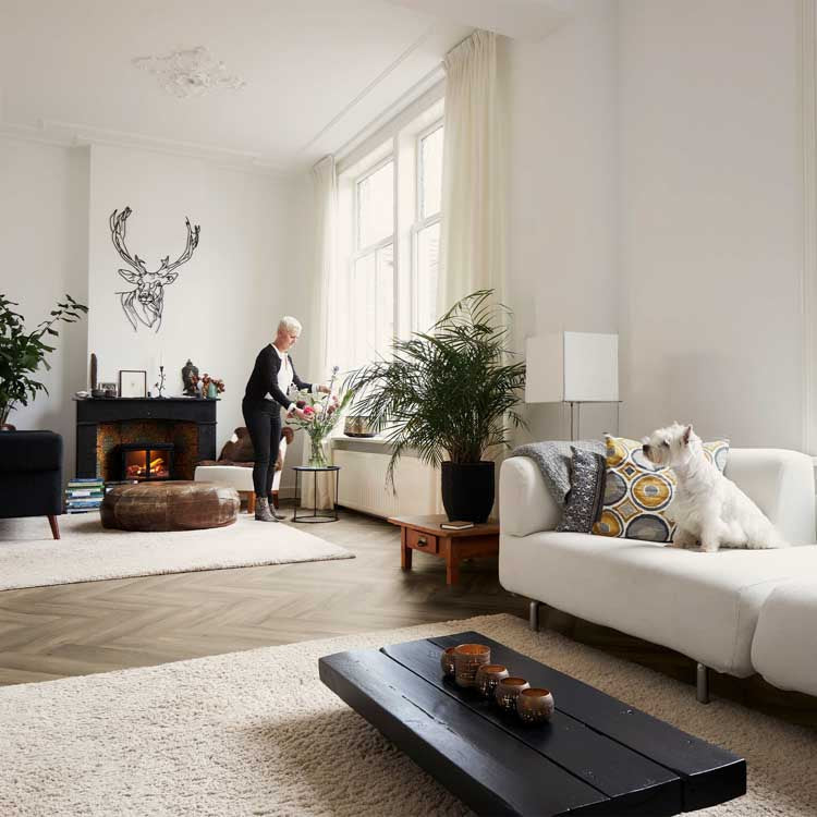 lichte eiken vloer in visgraat patroon met brede planken in een lichte, moderne woonkamer met witte muren, beige hoogpolig tapijt, lichte bank en groene planten