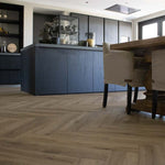 Visgraatvloer in licht beige eiken kleur met zichtbare houtnerfstructuur, gecombineerd met een moderne donkere keuken en een eettafel met beige beklede stoelen.