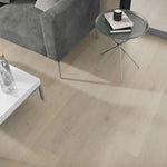 lichte vloer met brede planken in licht beige eiken kleur en subtiele houtstructuur, sfeervol interieur met een grijsgroene velours bank en ronde metalen bijzettafel