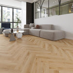 licht eiken visgraatvloer met natuurlijke houtstructuur en brede planken in een moderne lichte woonkamer met grote raampartij, beige-grijze hoekbank en ronde glazen salontafel met marmerlook sokkel