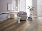 Licht bruin eiken vloer met brede planken en subtiele houtstructuur in een moderne lichte woonkamer met zachtgrijze fauteuil en marmeren bijzettafel.